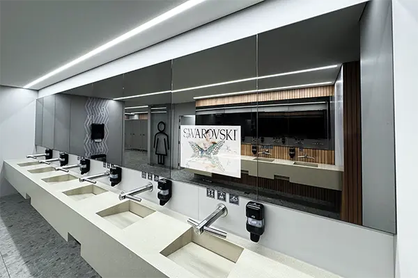 Zdjęcie łazienki w galerii handlowej z wyświetlanymi reklamami na lustrach ponad umywalkami.